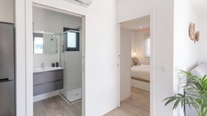 A modern apartment with a kitchen, a glass-enclosed shower, a bedroom with a bed and bedside lamp, and a living area with a plant. - Villa El Rincón de Lupe Torrox by Ruralidays (Málaga)