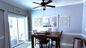 A dining area with a ceiling fan, a dining table with chairs, a large mirror, and a trash can. - First Floor Updated Coastal Summer Retreat at Magnolia Place - Pool View (Myrtle Beach)