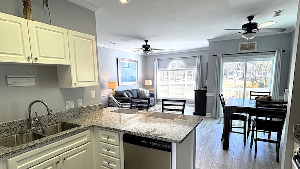 A modern kitchen with white cabinets, granite countertops, a built-in dishwasher, and a dining area with a table and chairs. - First Floor Updated Coastal Summer Retreat at Magnolia Place - Pool View (Myrtle Beach)