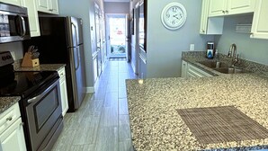 A kitchen with white cabinets, a granite countertop, and a stainless steel refrigerator. - First Floor Updated Coastal Summer Retreat at Magnolia Place - Pool View (Myrtle Beach)