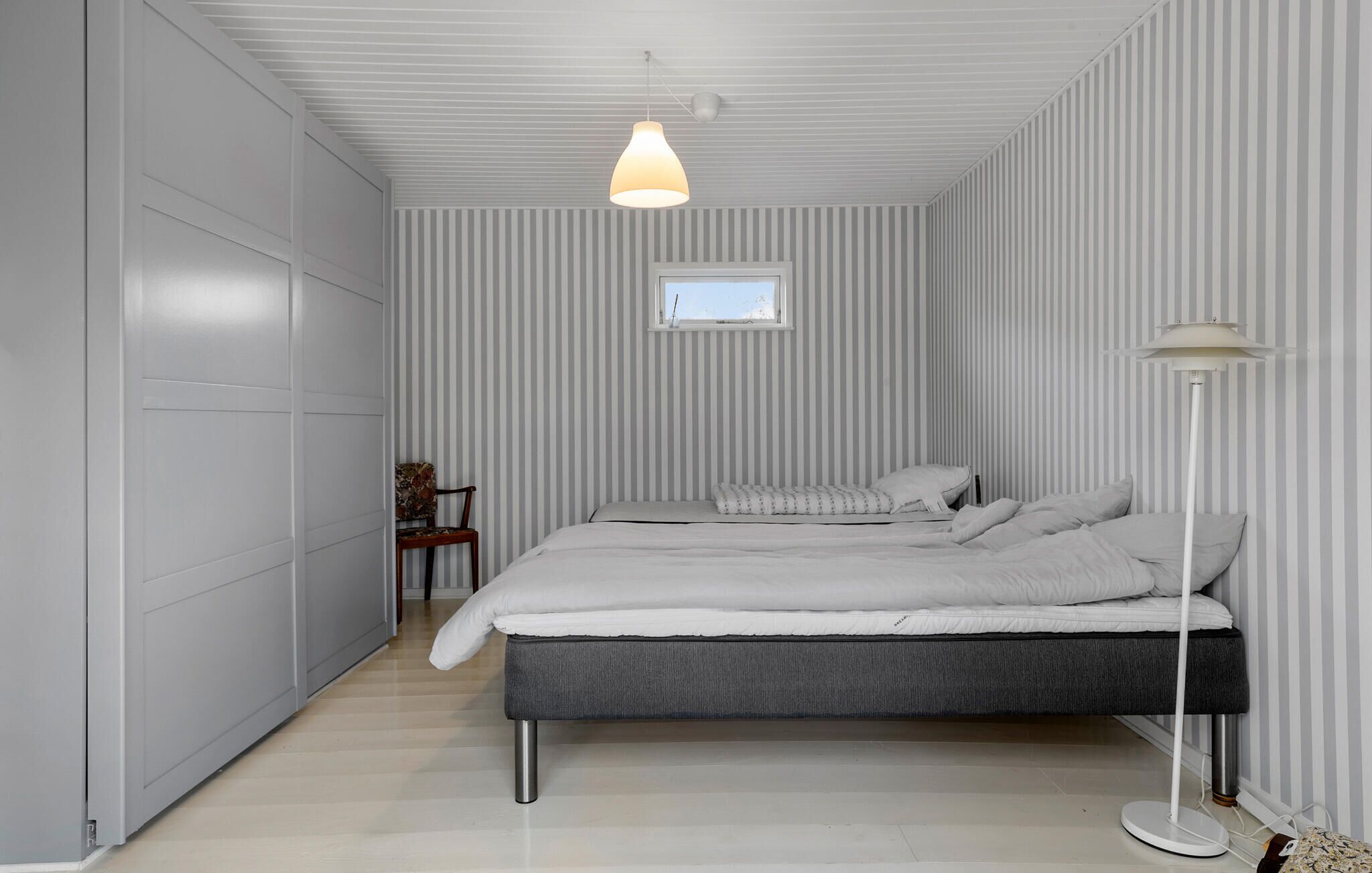 Een moderne slaapkamer met een bed, een stoel, een vloerlamp en een raam.