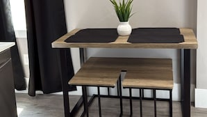 Een eetgedeelte met een houten tafel en bank, een potplant en een wanddecoratie.