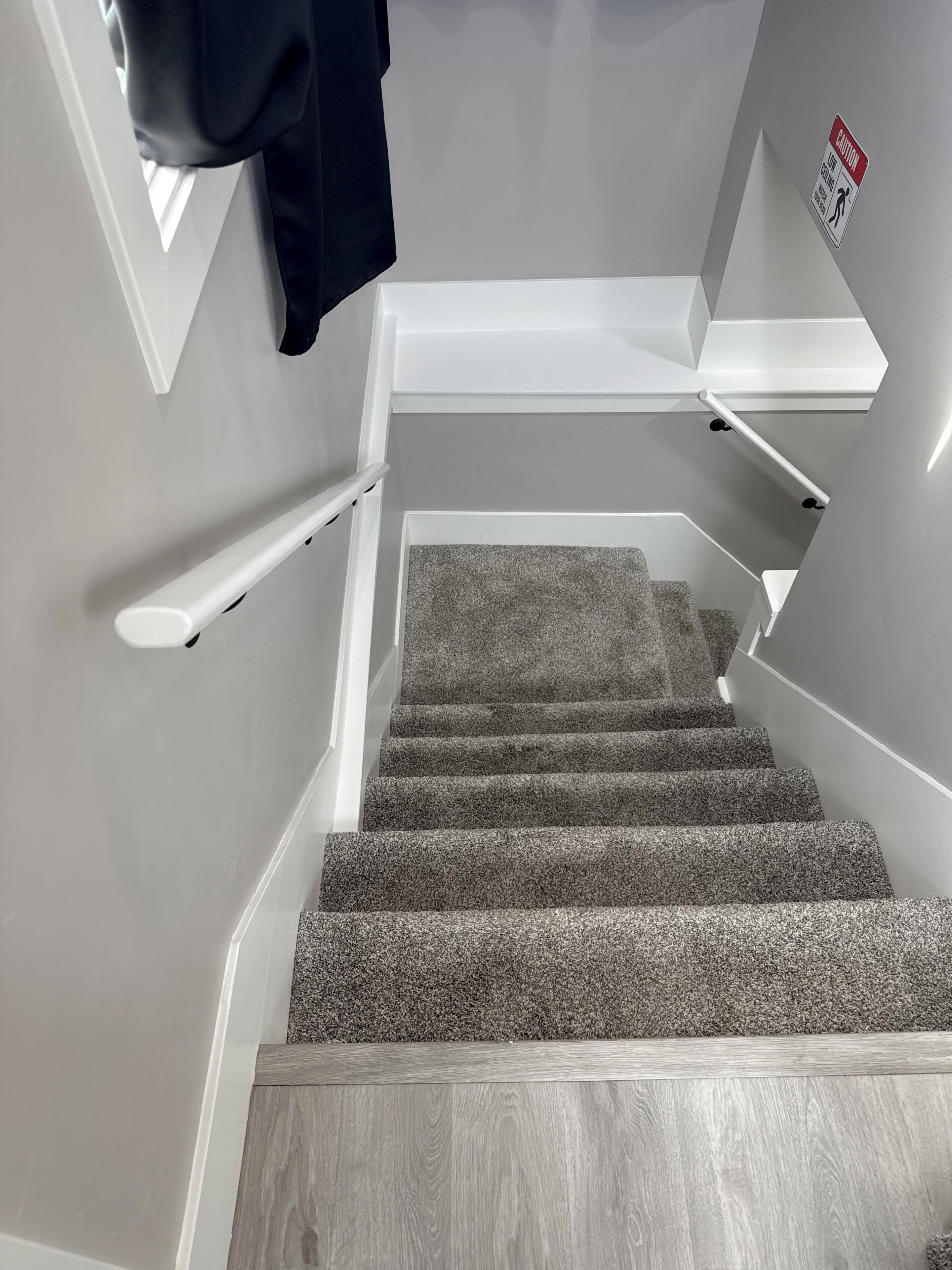 Una escalera con escalones alfombrados, barandillas blancas y un letrero de precaución en la pared.