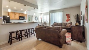 Una sala de estar moderna con un sofá marrón, una mesa de centro y una cocina con armarios de madera y un microondas.