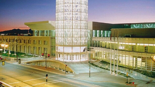 Un edificio moderno con una torre cilíndrica de vidrio, un cuerpo anexo de techo plano y una estructura de varios niveles con grandes ventanales.