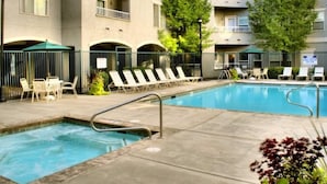 Una piscina con sillas de descanso y sombrillas, rodeada de un edificio con balcones y árboles.
