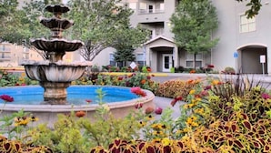 Un patio con una fuente de varios niveles rodeado de flores coloridas y un edificio con el rótulo 'CITIFRONT'.