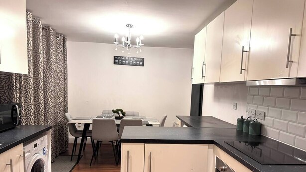 A compact kitchen with a washing machine, a dining area with a table and chairs, and a coffee menu sign.