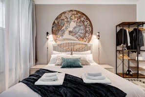 A hotel room with a bed, a headboard with a decorative panel, a wardrobe, and a bedside table with a lamp.