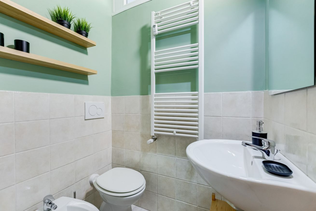 A bathroom with a toilet, sink, towel rack, and shelves with plants.