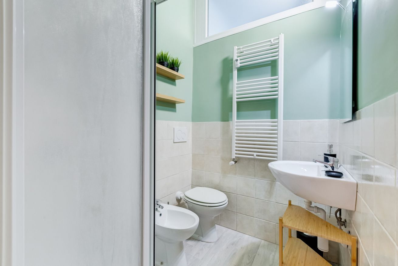 Un bagno con il water, bidet, lavandino, porta asciugamani e mensole con piante.