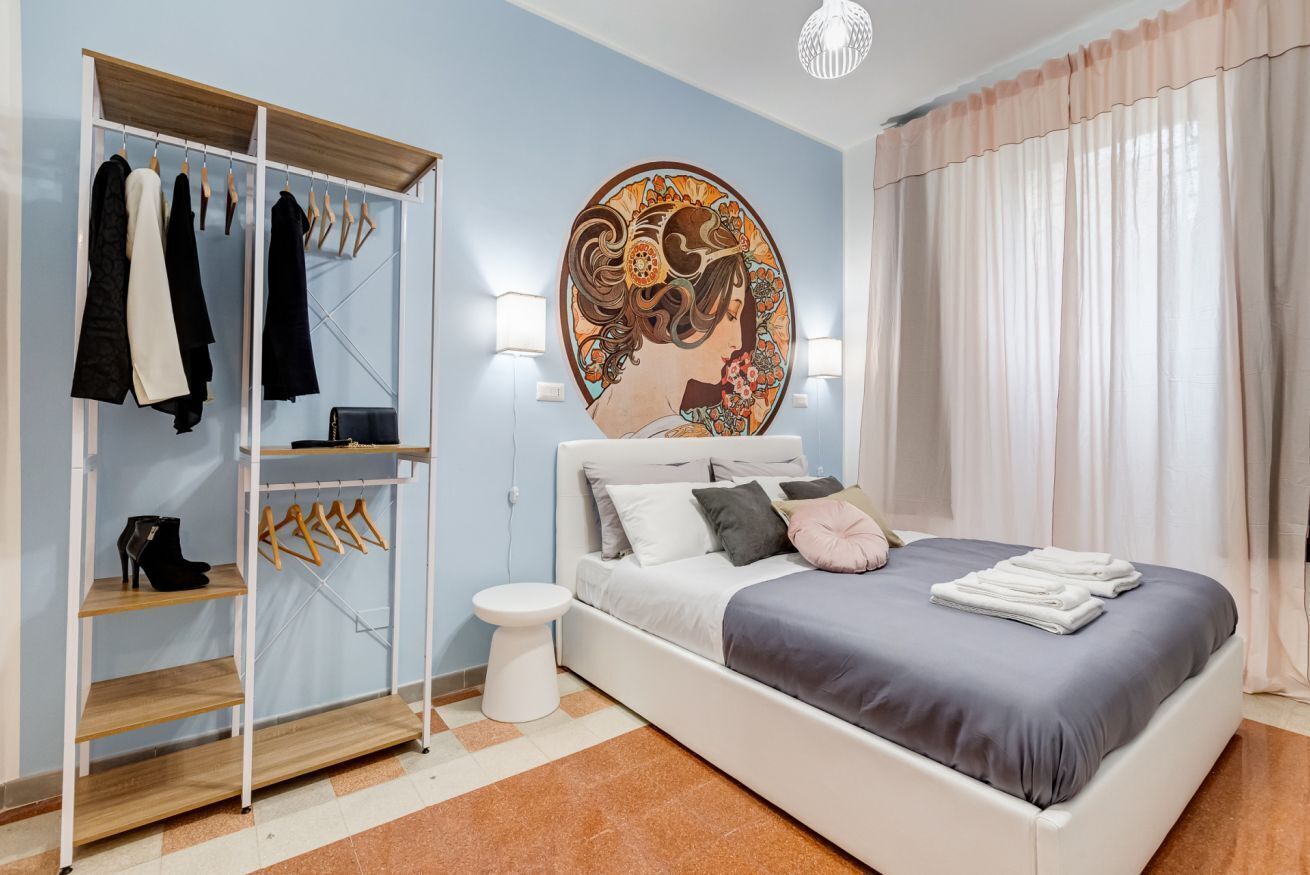 Un dormitorio con cama, armario, un cuadro y mesita de noche.