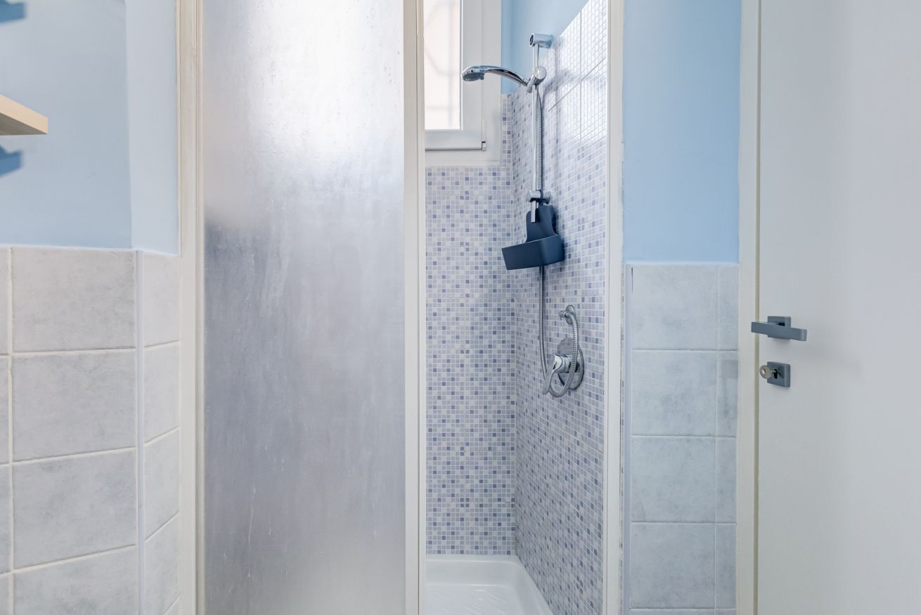 Ducha con cabezal de ducha de mano, grifo empotrado en la pared y una pequeña ventana sobre la ducha.