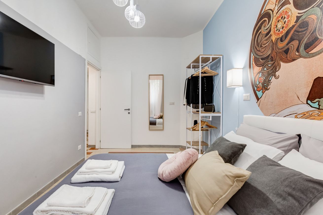 Een hotelkamer met een bed, een televisie, een kledingkast en een muurschildering.