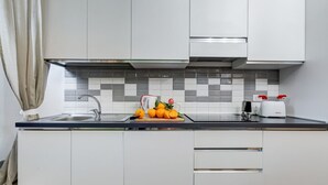 Una cocina moderna con salpicadero de azulejos, un lavamanos y una encimera con una tabla de cortar que sostiene naranjas.