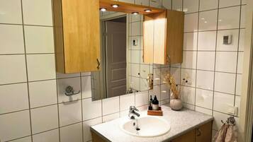 A bathroom with white tiled walls, a wooden vanity with a sink, a mirror, and a towel rack.