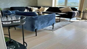 A modern living room with a black sofa, a blue armchair, and a coffee table. There is a large window offering a view of the outdoors. - Free Parking Space, Balcony, Prime Location (Ålesund)