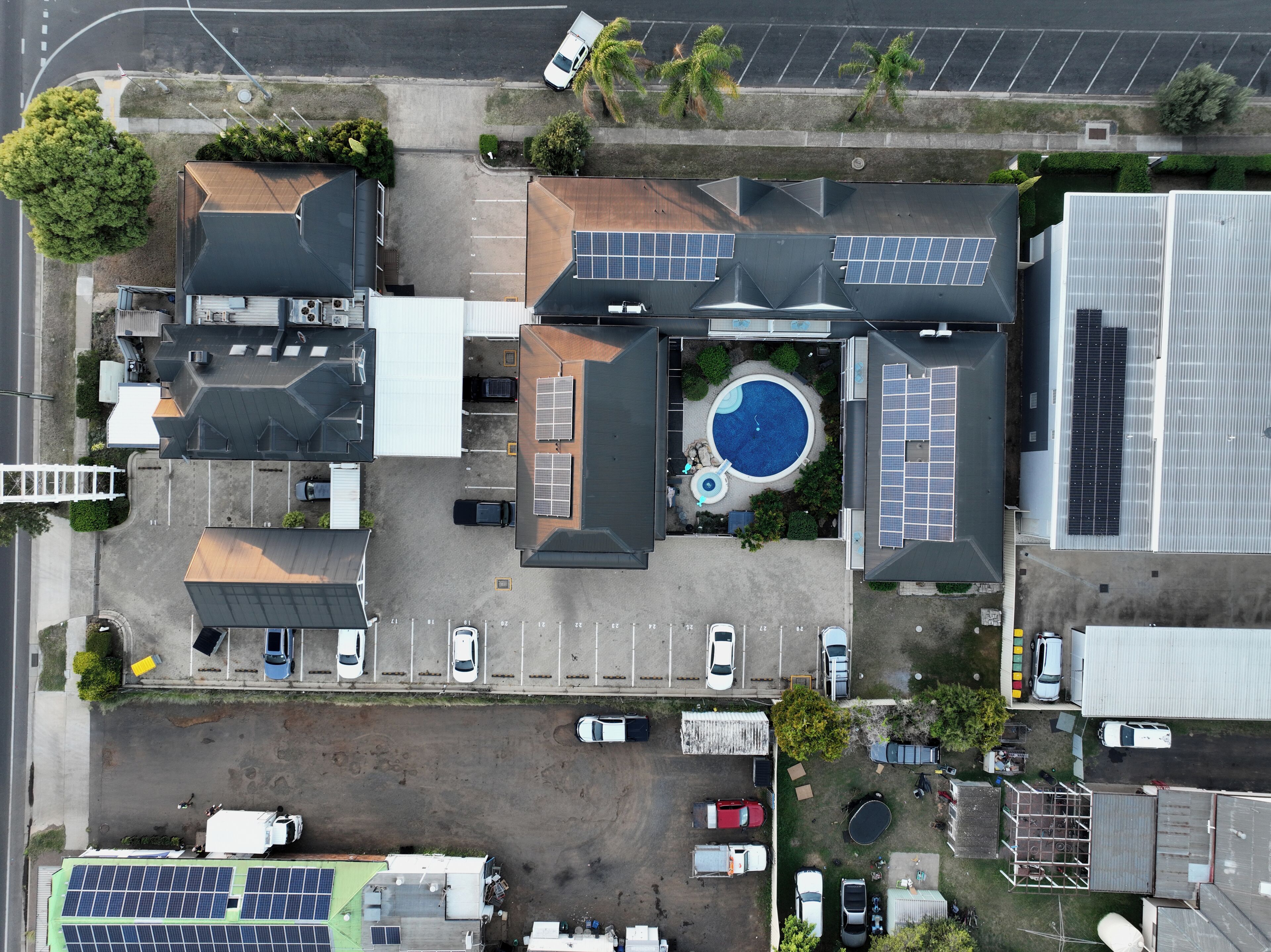 An aerial view of a residential area with multiple houses, a swimming pool, and solar panels.