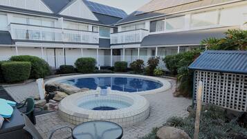 A swimming pool with a hot tub, surrounded by a patio area with chairs and a table.