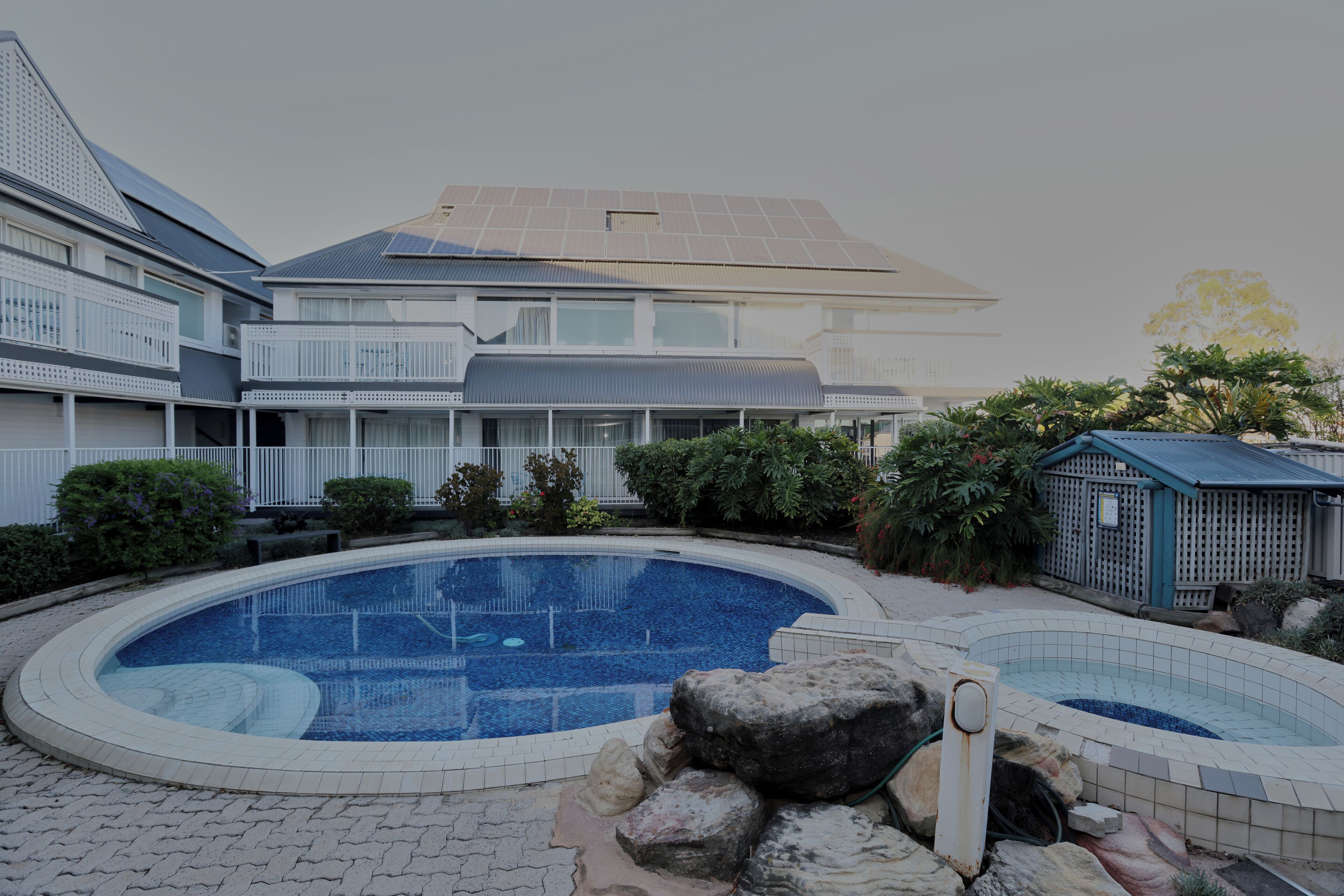 A residential building with a swimming pool, a covered patio, and a small garden area.