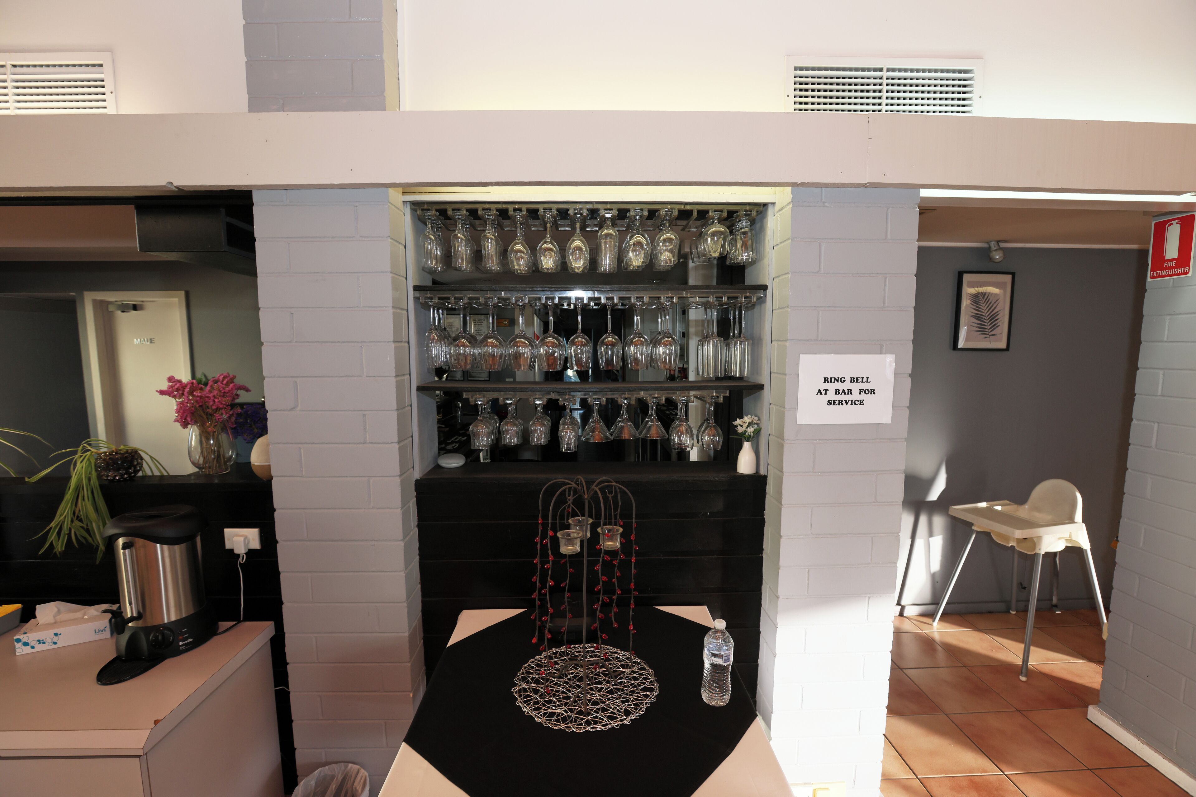 A bar area with a shelf of glassware, a coffee machine, and a chair.