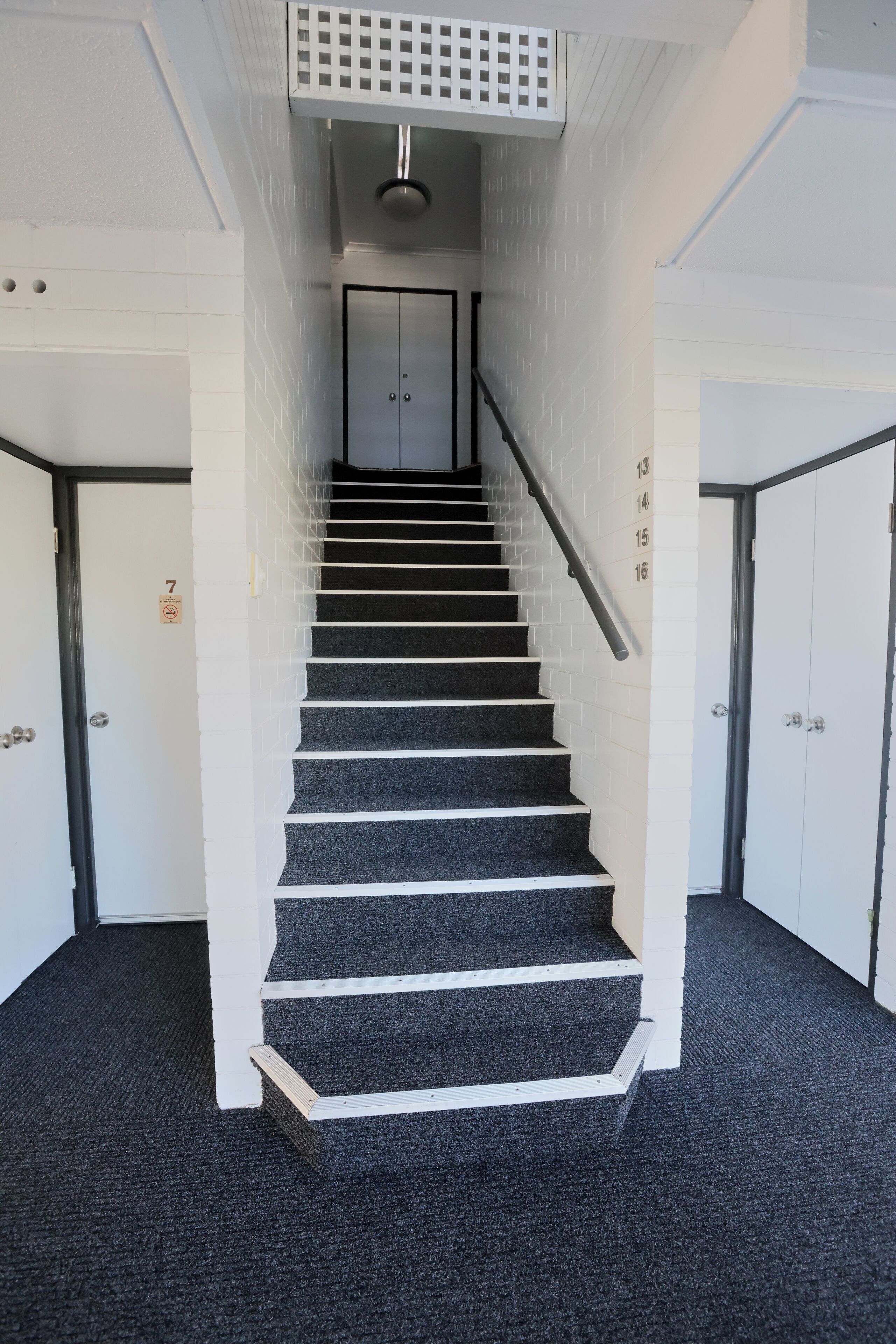 A staircase with a handrail, carpeted steps, and white walls.
