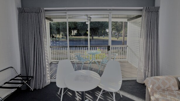 A balcony with a table and chairs, a sofa, and a view of a park and street. - Dalby Manor Motor Inn  (Dalby)