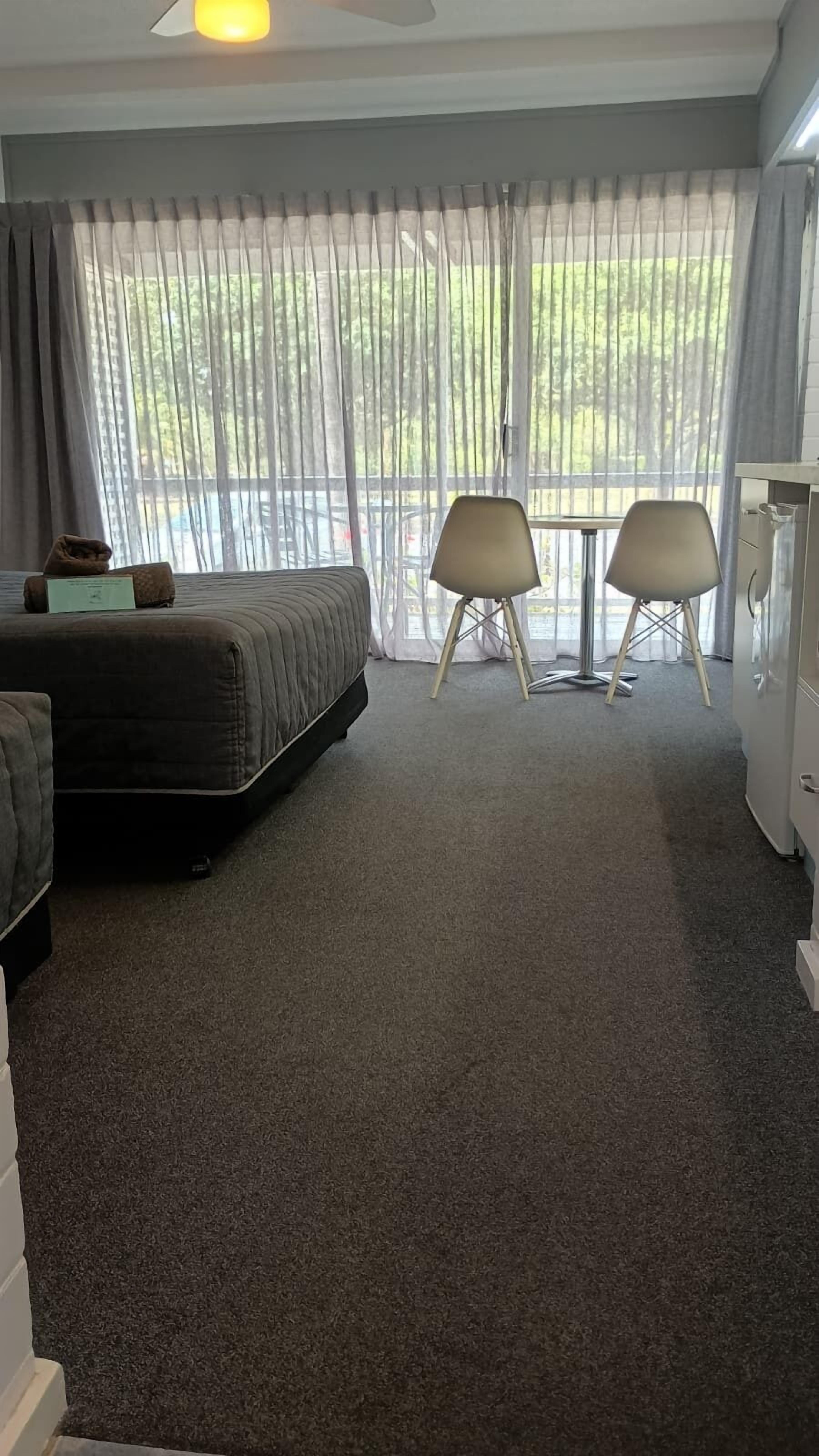 A hotel room with a bed, two chairs, a small table, and a refrigerator.