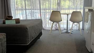 A hotel room with a bed, two chairs, a small table, and a refrigerator.