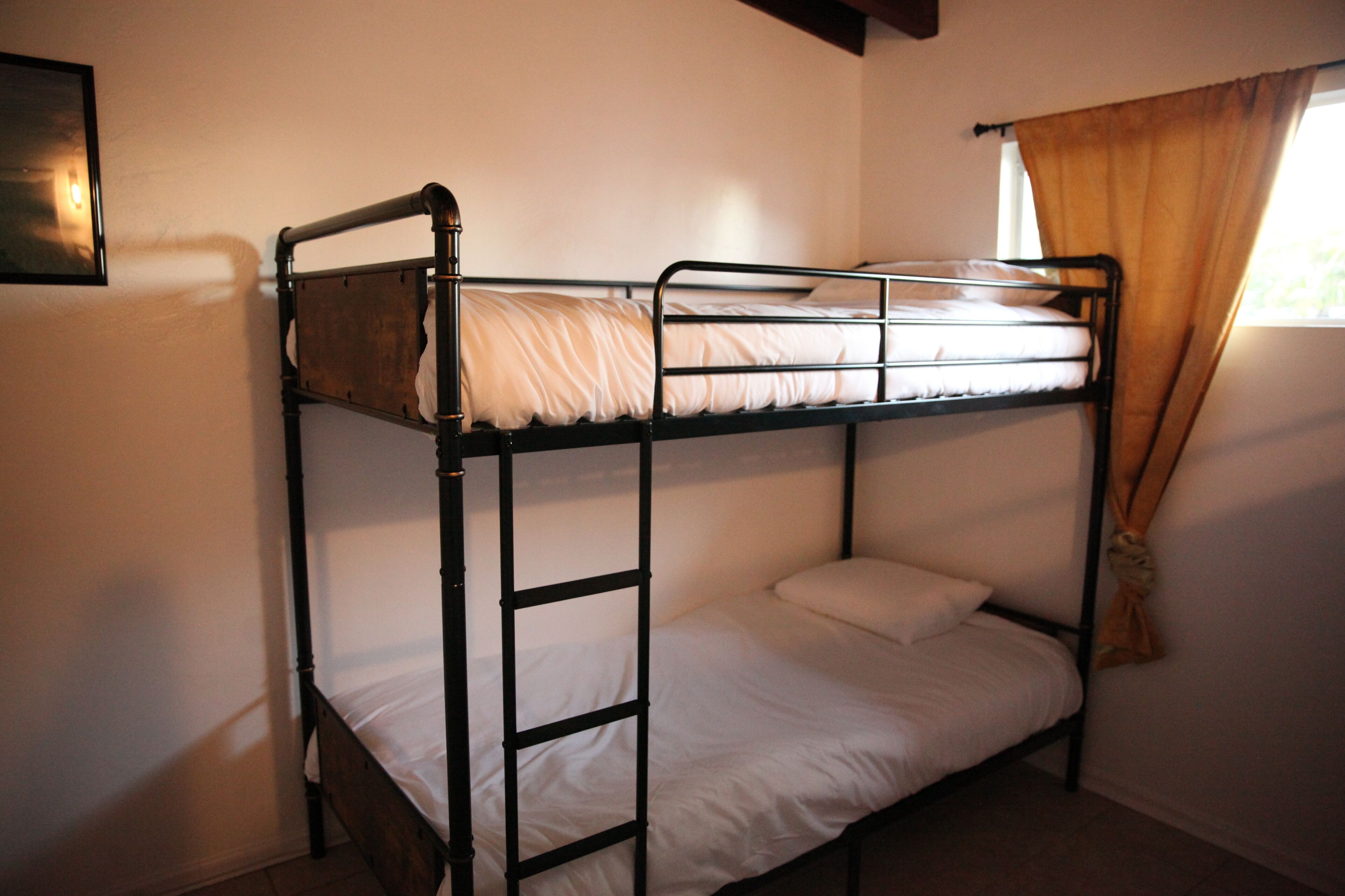 Una cama litera con una escalera, una cama individual debajo y una ventana con cortinas.