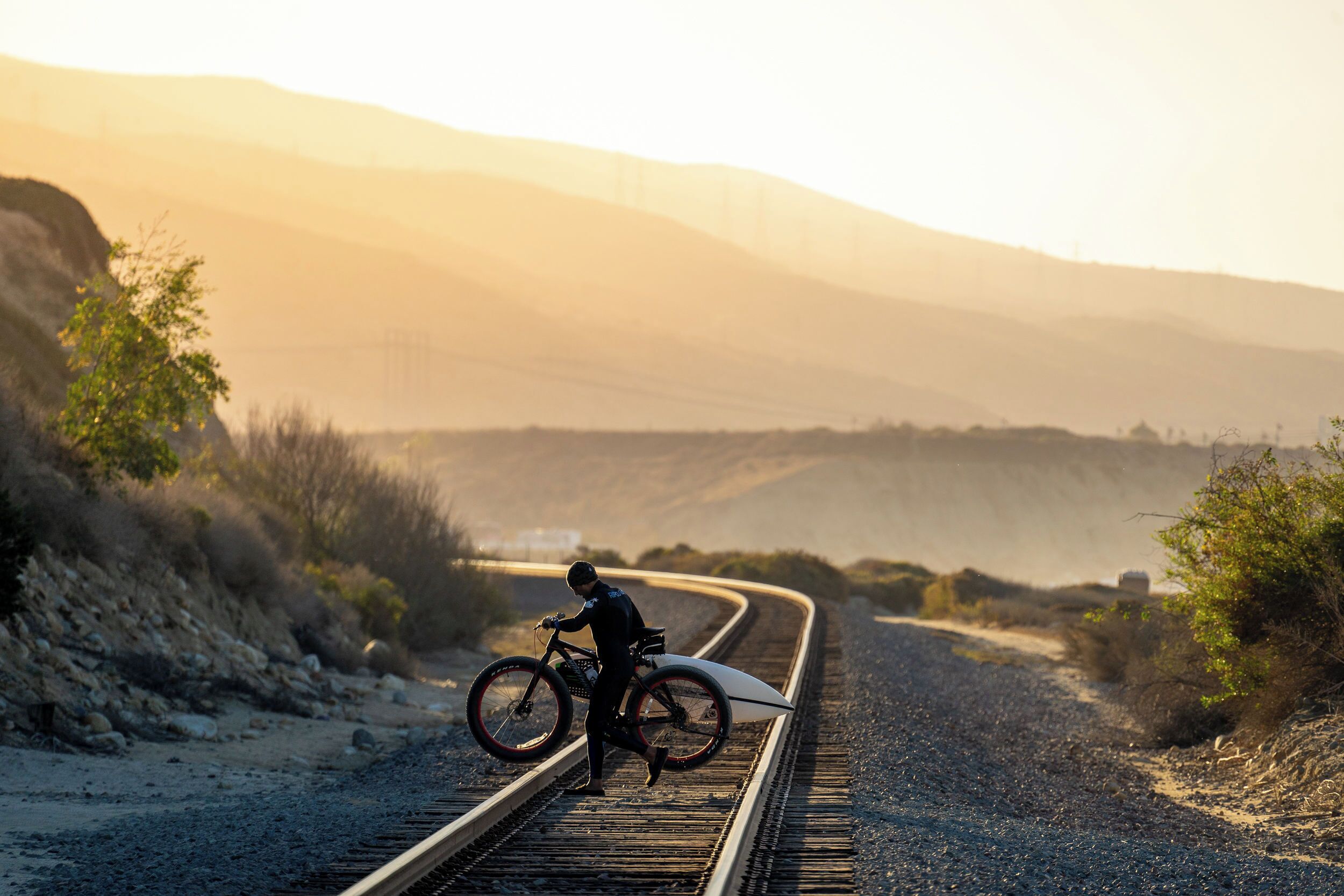 Une personne à vélo, transportant une planche de surf, se trouve sur une voie ferrée.