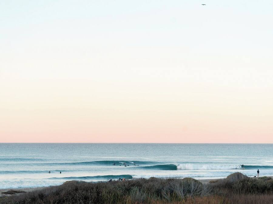 Une plage avec des vagues, un phare et une personne debout sur le rivage.