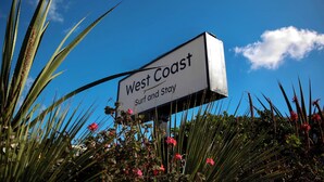 Un letrero con el texto 'West Coast Surf and Stay' sobre un cielo azul despejado.