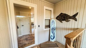 A wooden porch with a woven doormat, a wooden bench, a decorative fish, and a door leading to an interior space.