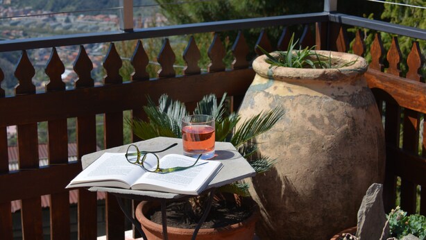 Ein Balkon mit Holzwertkasten, einem Blumentopf, einem Getränk und einem offenen Buch.