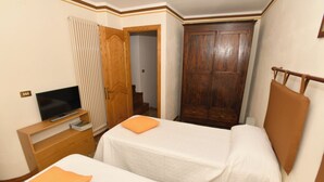 Ein Hotelzimmer mit zwei Betten, einem Holzschrank, einem Fernseher auf einem Holztisch und einem Fenster mit Jalousien.