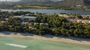 A coastal resort with a large hotel, dense greenery, and a beach.