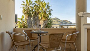 Ein Balkon mit Korbstühlen und einem Tisch, mit Blick auf Palmen und ein Gebirge.