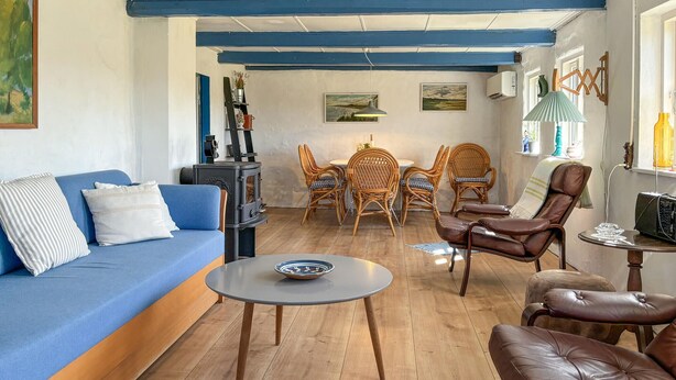Un salon chaleureux avec un canapé bleu, des fauteuils en osier, une table ronde et un plancher en bois.