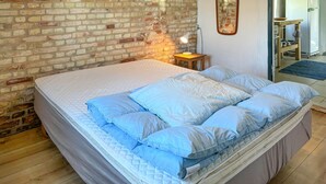 Une chambre avec un mur en briques, un lit avec une literie bleue, une lampe de chevet et un miroir sur le mur.