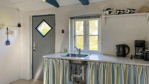 Une cuisine avec un rideau à rayures, un évier, une fenêtre et une machine à café.