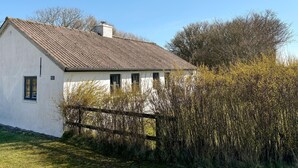 Un bâtiment blanc avec un toit en pente et une cheminée, entouré d’arbres et d’une clôture.
