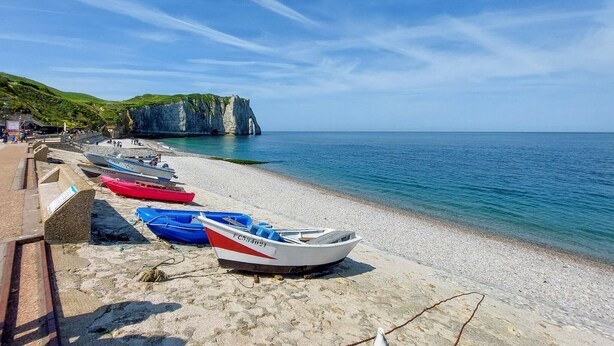 A beach with boats lined up on the shore, a clear sky, and a cliff in the background.