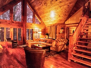 A cozy log cabin interior with a wooden staircase, large windows, and a fireplace. - You’ve Found Paradise With this  Spacious Log Cabin on Keuka Lake - (Branchport)
