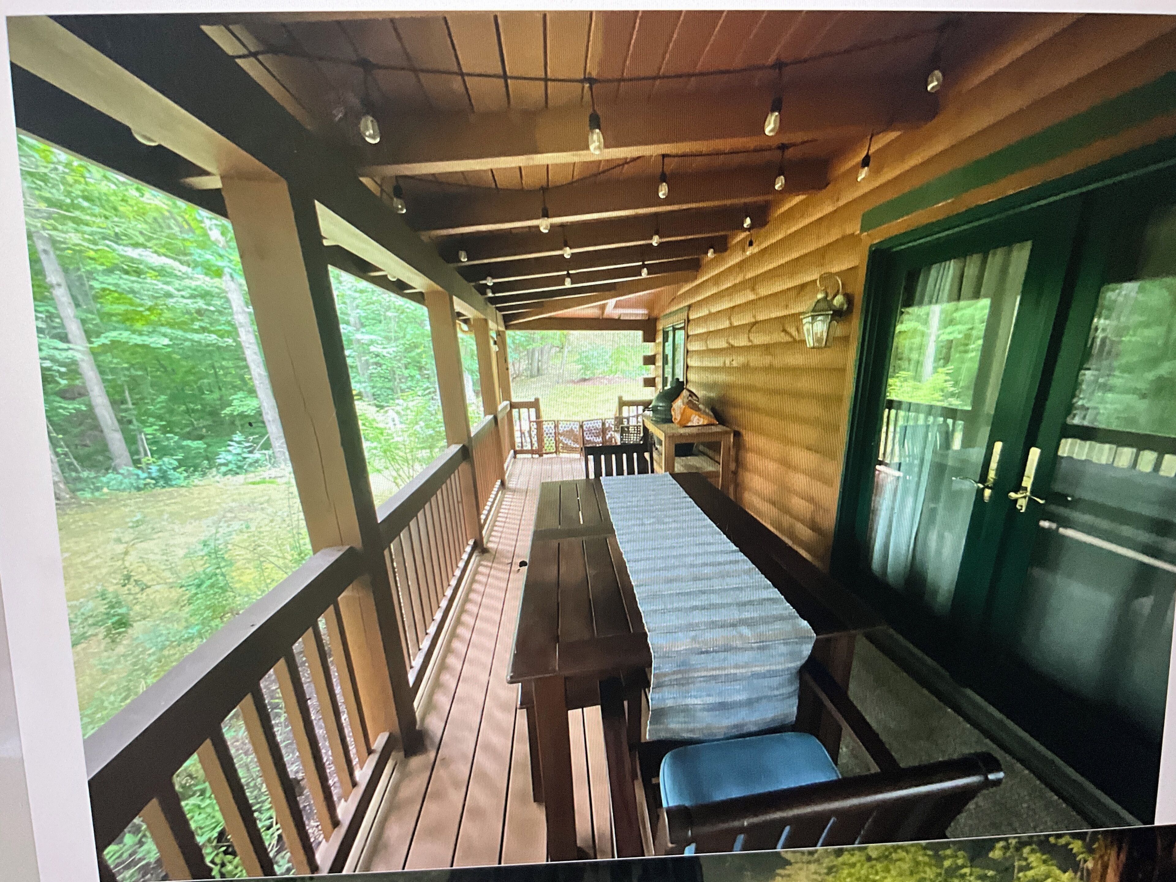 A covered porch with a wooden table and chairs, a bench, and a view of the surrounding forest.