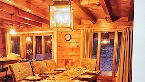 A wooden dining room with a table set for six, large windows, and a clock on the wall.