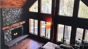 A cabin with a stone fireplace, large windows, and a wooden ceiling.