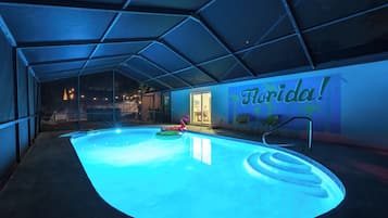 An indoor swimming pool with a glass ceiling, a 'Florida!' sign on the wall, and a poolside chair.