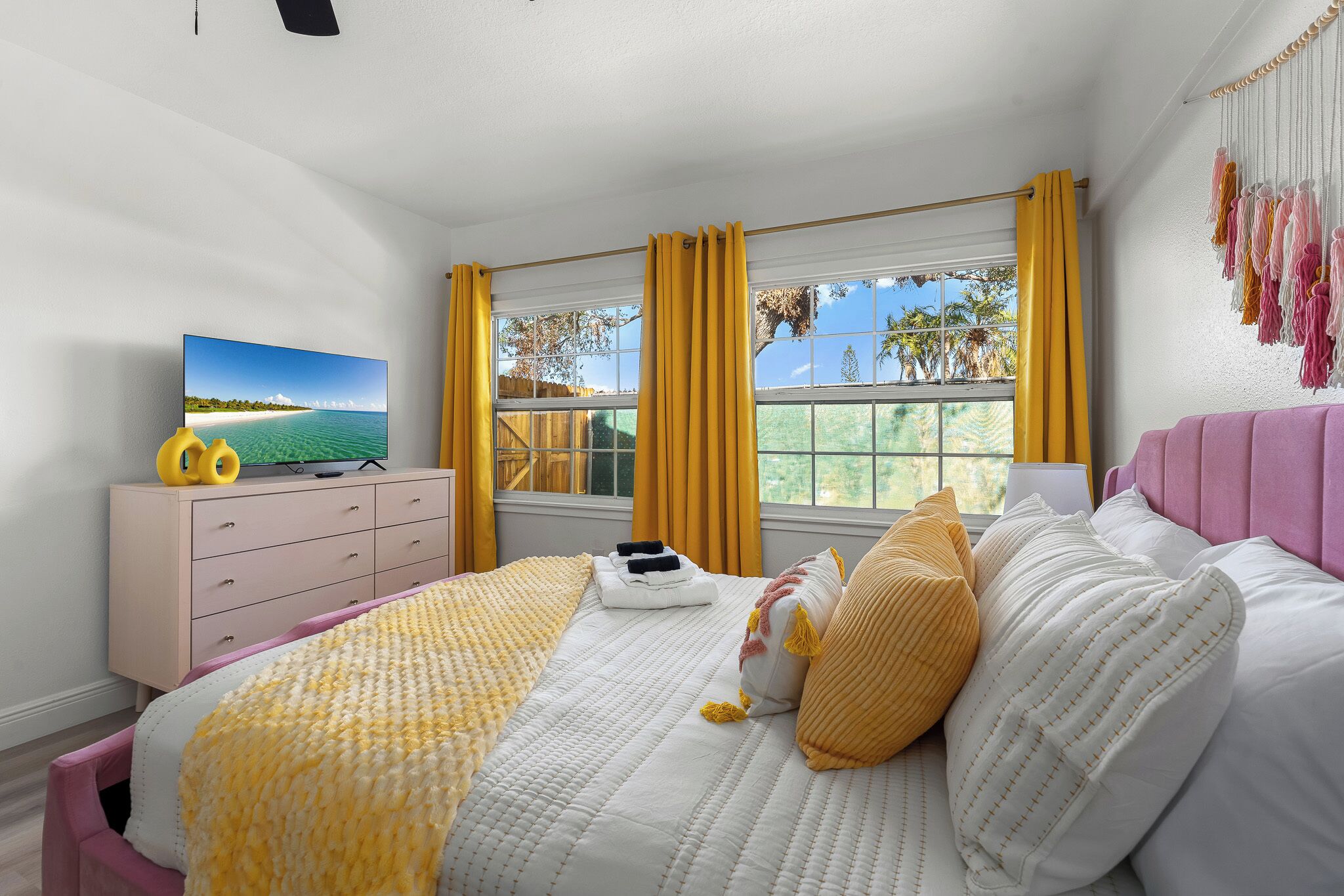 A bedroom with a bed, a dresser, a TV, and a window with curtains.