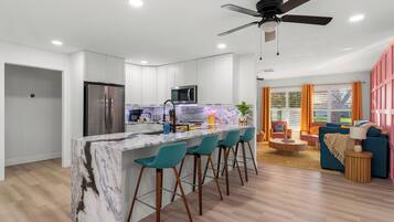 A modern kitchen with a marble island, bar stools, a refrigerator, and a microwave.